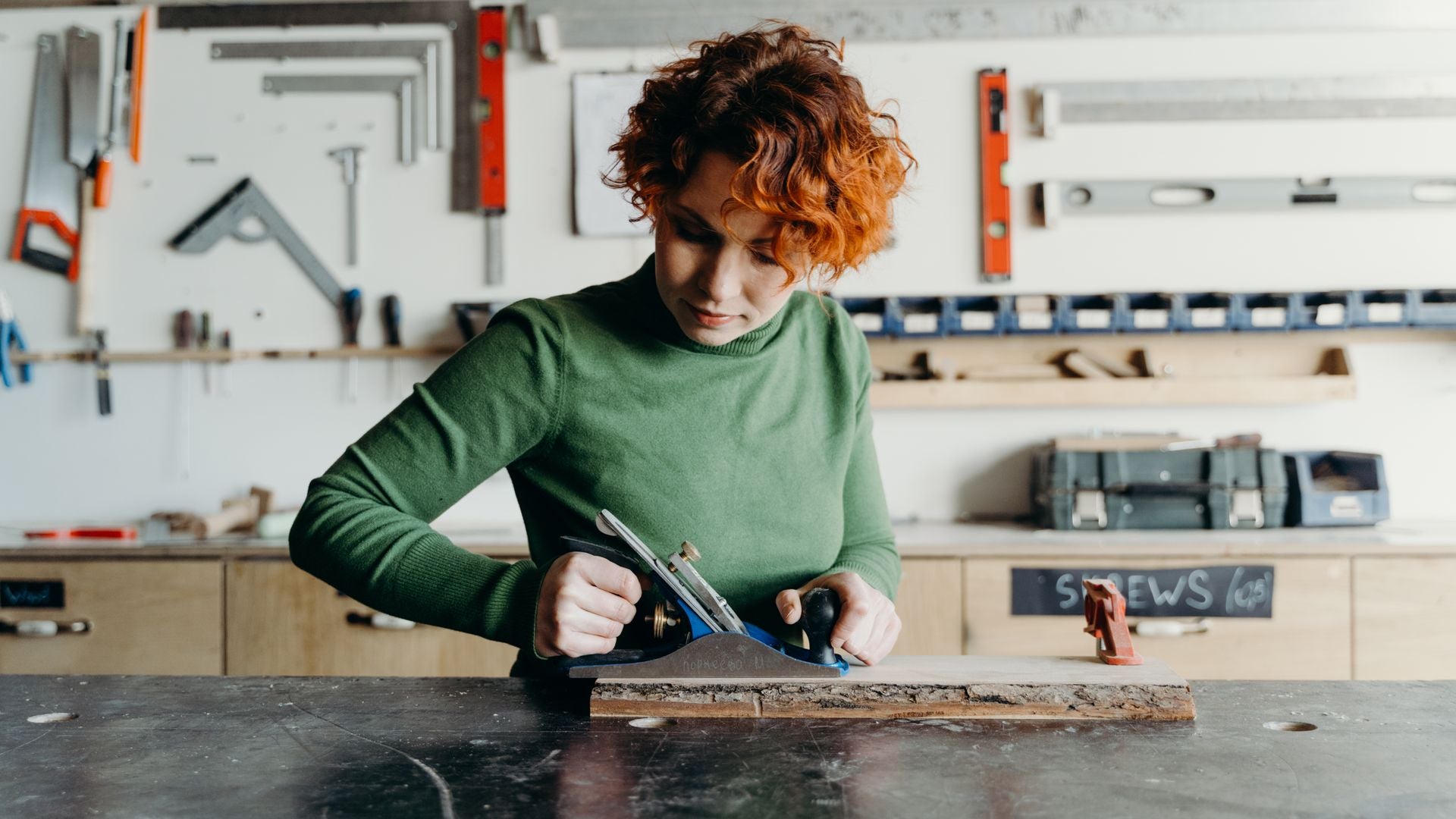 Woman using a hand plane at a woodworking bench